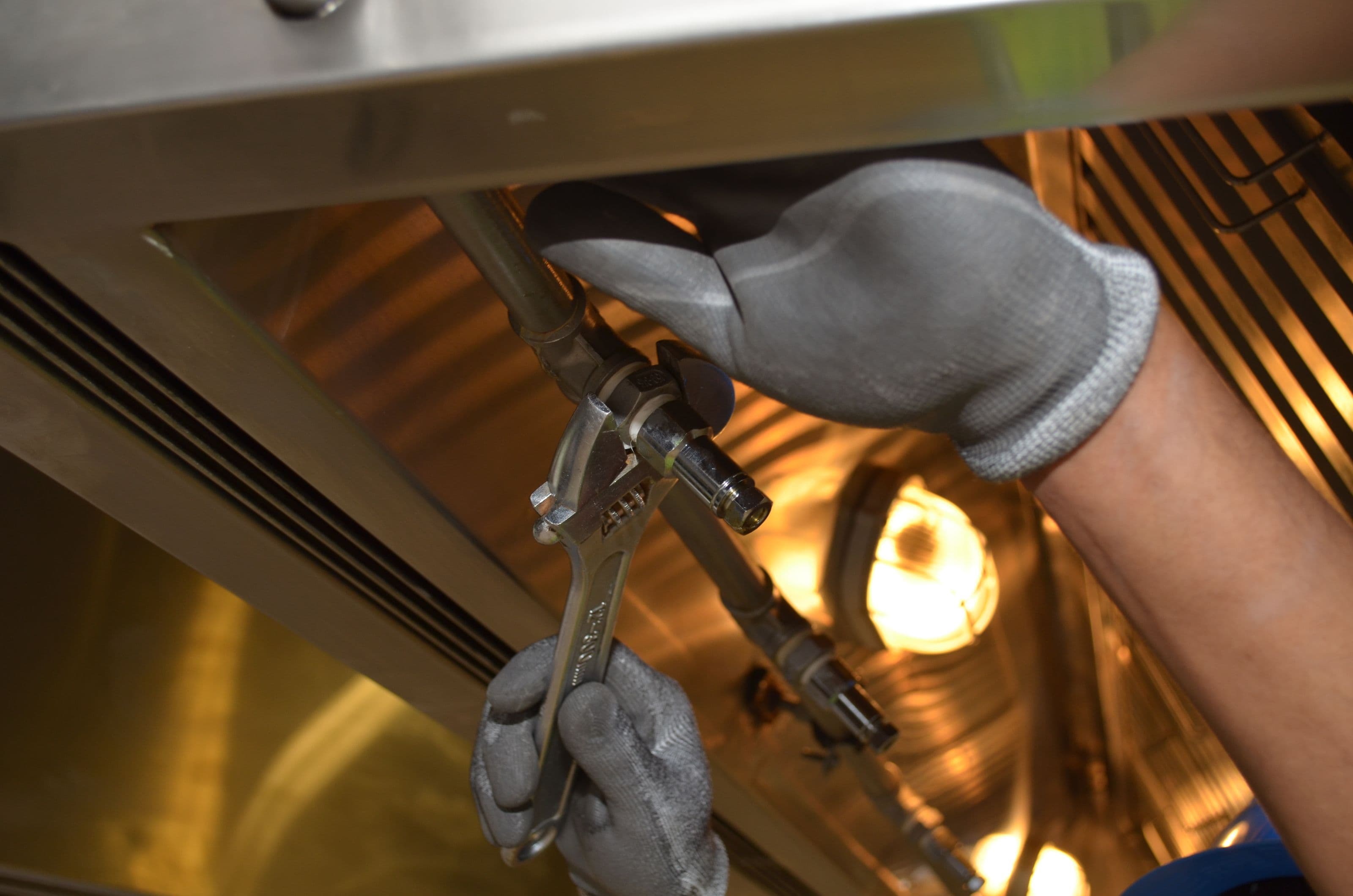 Plumber using a spanner to work on pipe fittings beneath a sink